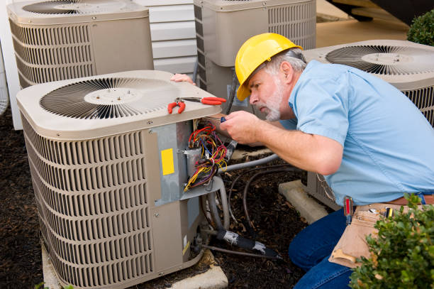 HVAC technician in yellow hard hat repairing an outdoor air conditioning unit